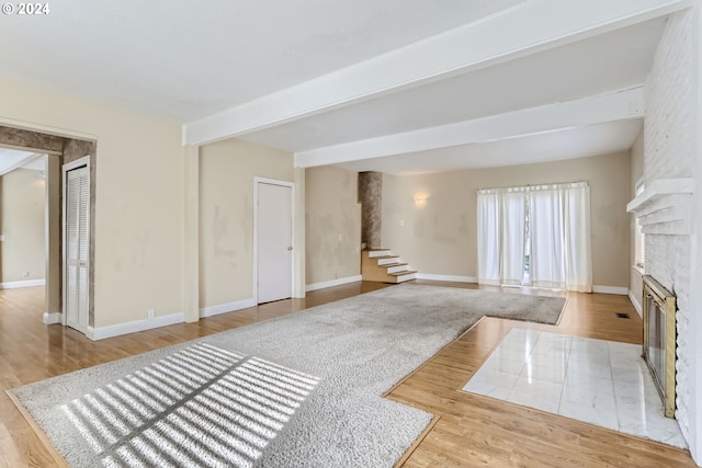 living room featuring light wood-type flooring, a large fireplace, and beamed ceiling