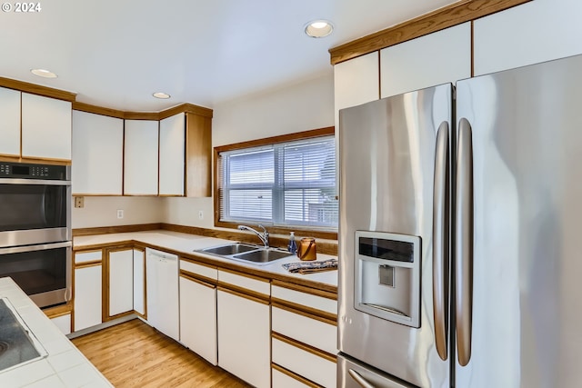 kitchen with white cabinetry, sink, appliances with stainless steel finishes, light hardwood / wood-style flooring, and tile counters