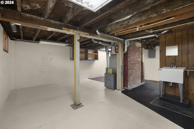 basement featuring wood walls, sink, electric panel, and heating unit