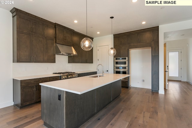 kitchen featuring sink, hanging light fixtures, wall chimney range hood, dark hardwood / wood-style flooring, and an island with sink