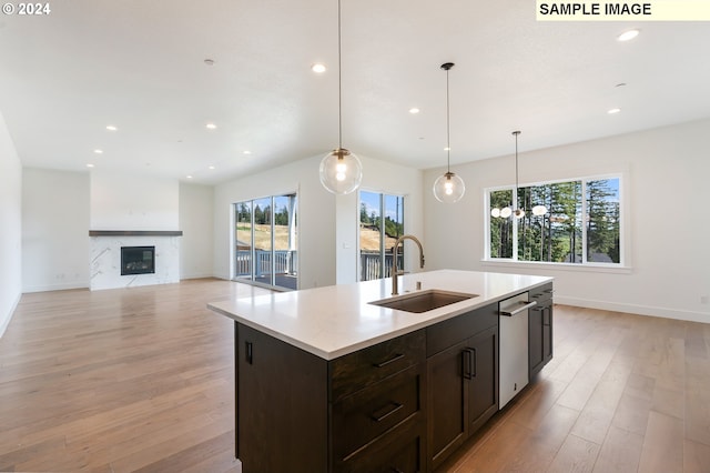 kitchen featuring a kitchen island with sink, a high end fireplace, hanging light fixtures, sink, and light hardwood / wood-style flooring