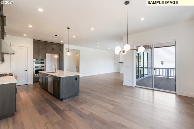 kitchen with hardwood / wood-style floors, a kitchen island with sink, sink, decorative light fixtures, and stainless steel appliances