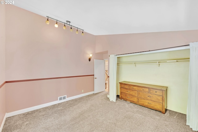 unfurnished bedroom featuring vaulted ceiling, light colored carpet, track lighting, and a closet