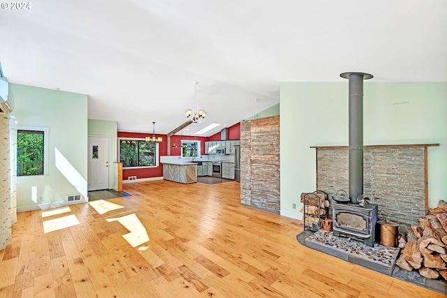 living room with lofted ceiling, a wood stove, an inviting chandelier, and light hardwood / wood-style flooring