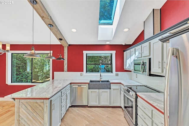 kitchen featuring sink, decorative light fixtures, appliances with stainless steel finishes, kitchen peninsula, and light hardwood / wood-style floors