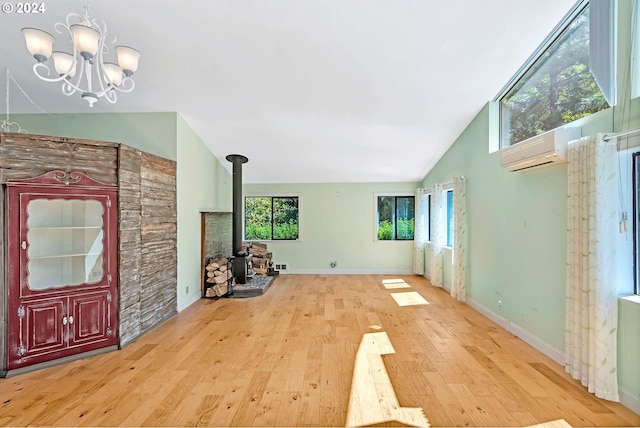 unfurnished living room with an inviting chandelier, high vaulted ceiling, a wood stove, a wall unit AC, and light hardwood / wood-style floors