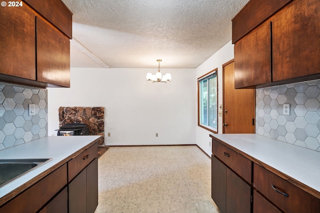 kitchen with an inviting chandelier, sink, a textured ceiling, tasteful backsplash, and decorative light fixtures