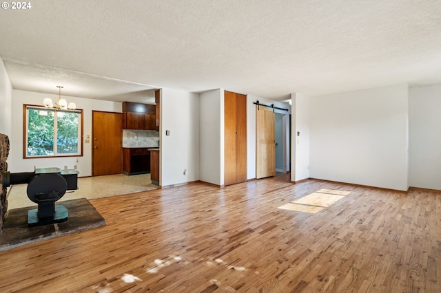 living room featuring a barn door, light wood-type flooring, a textured ceiling, and an inviting chandelier