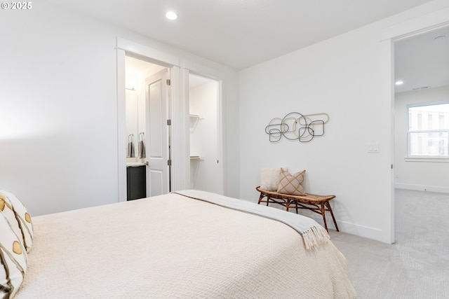 bedroom with a walk in closet, light colored carpet, and connected bathroom