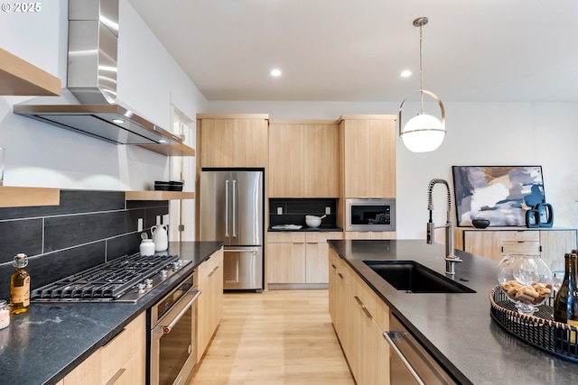 kitchen with pendant lighting, sink, light brown cabinets, stainless steel appliances, and wall chimney range hood