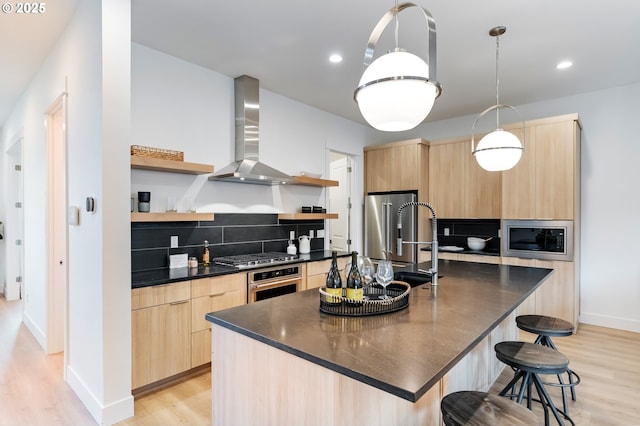 kitchen with appliances with stainless steel finishes, tasteful backsplash, a center island with sink, decorative light fixtures, and wall chimney exhaust hood