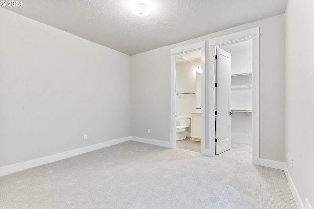 unfurnished bedroom featuring a spacious closet, a textured ceiling, connected bathroom, light carpet, and a closet