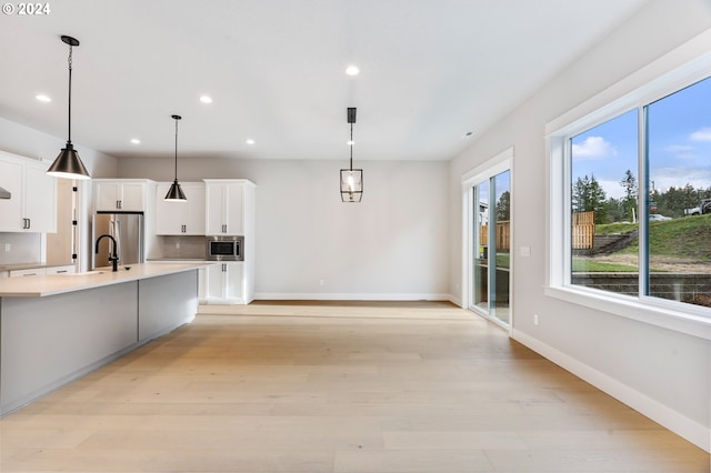 kitchen featuring light wood-type flooring, white cabinetry, hanging light fixtures, and appliances with stainless steel finishes