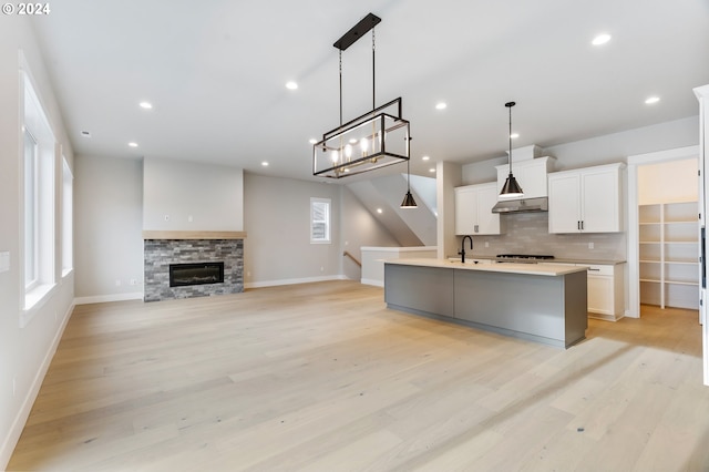 kitchen with a kitchen island with sink, white cabinetry, pendant lighting, and light hardwood / wood-style floors