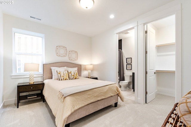 bedroom with a walk in closet, light colored carpet, and ensuite bathroom