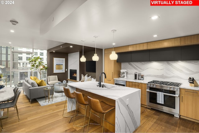 kitchen featuring sink, light hardwood / wood-style flooring, gas range, a center island with sink, and pendant lighting