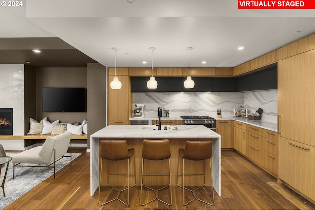 kitchen featuring decorative light fixtures, a fireplace, a center island with sink, dark wood-type flooring, and a breakfast bar area