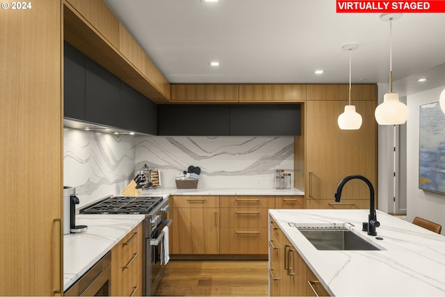 kitchen with decorative light fixtures, hardwood / wood-style flooring, high end range, sink, and light stone counters