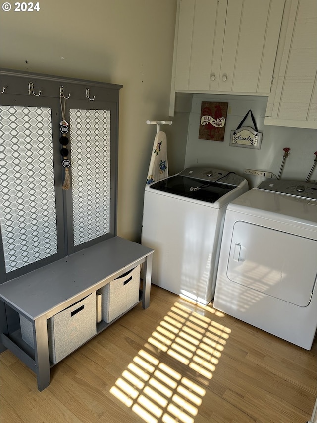 laundry room featuring washing machine and clothes dryer, light wood-type flooring, and cabinets