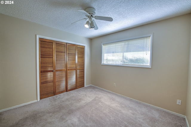 unfurnished bedroom featuring a textured ceiling, a closet, light colored carpet, and ceiling fan