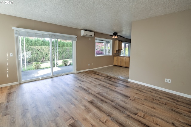 unfurnished living room with a textured ceiling, ceiling fan, a wall mounted air conditioner, and light wood-type flooring