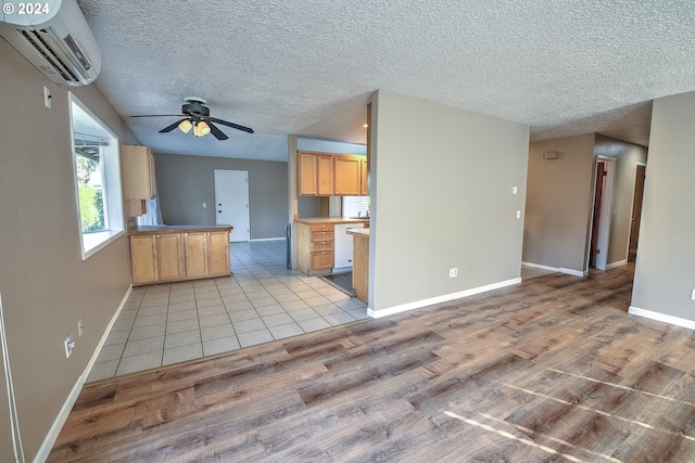 kitchen with kitchen peninsula, a textured ceiling, a wall unit AC, ceiling fan, and light hardwood / wood-style floors