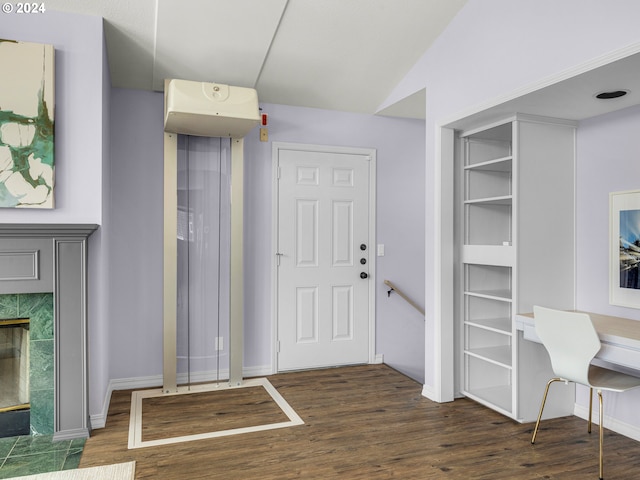 entryway with lofted ceiling, a tiled fireplace, dark wood-type flooring, and elevator