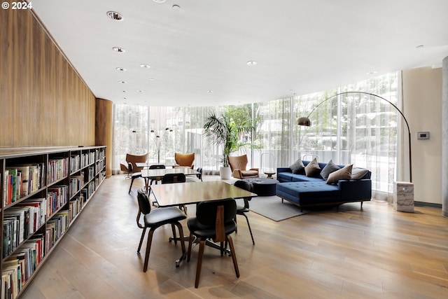 dining room with light hardwood / wood-style floors, a wall of windows, wooden walls, and a healthy amount of sunlight