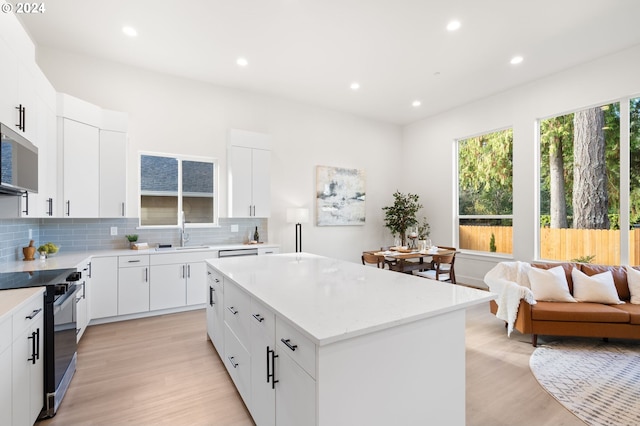 kitchen with light hardwood / wood-style floors, appliances with stainless steel finishes, backsplash, a kitchen island, and white cabinets