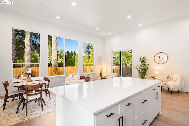 kitchen with white cabinets, light wood-type flooring, a healthy amount of sunlight, and a kitchen island