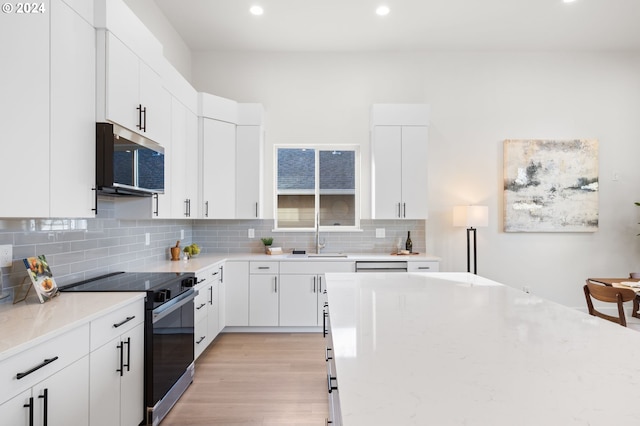 kitchen featuring white cabinetry, light stone counters, appliances with stainless steel finishes, backsplash, and light wood-type flooring