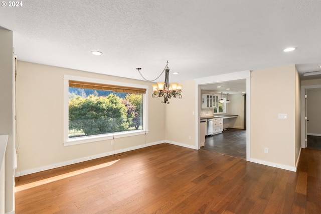 unfurnished dining area featuring dark wood-type flooring, a textured ceiling, and a notable chandelier