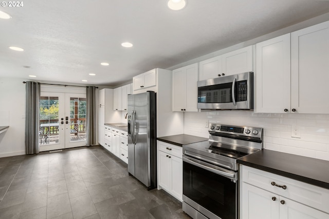 kitchen featuring french doors, dark tile patterned flooring, backsplash, white cabinetry, and appliances with stainless steel finishes