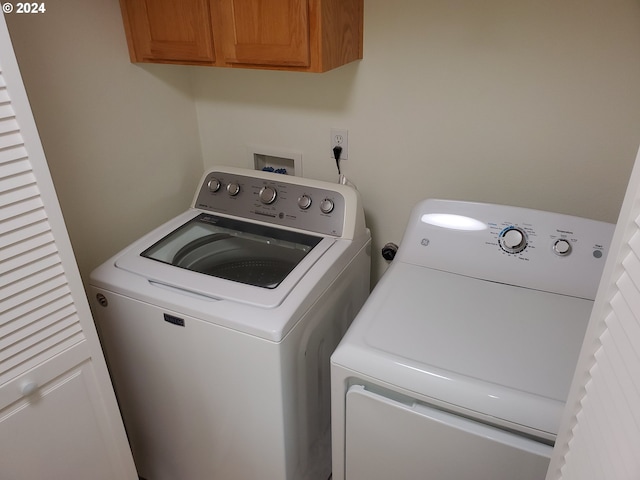 clothes washing area with separate washer and dryer and cabinets