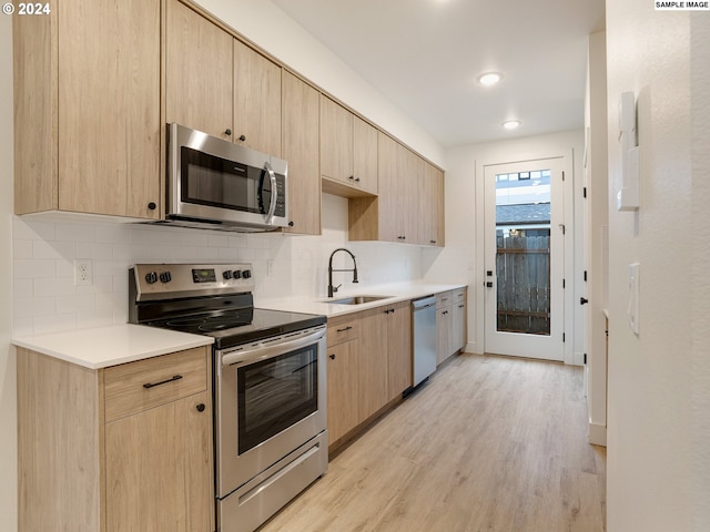 kitchen featuring decorative backsplash, appliances with stainless steel finishes, light brown cabinetry, sink, and light hardwood / wood-style flooring