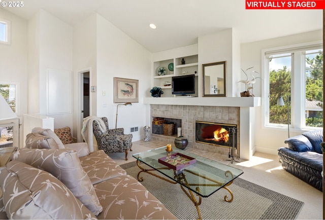 carpeted living room featuring built in shelves, high vaulted ceiling, and a tiled fireplace