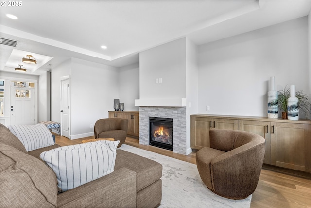 living room featuring a fireplace, light wood-type flooring, and a raised ceiling