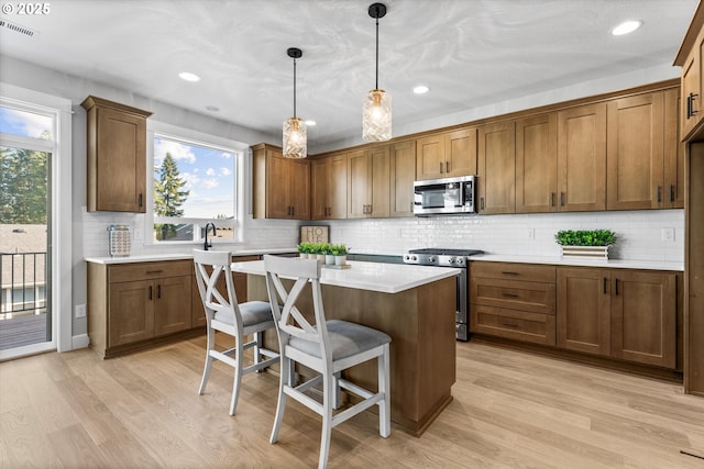 kitchen featuring light hardwood / wood-style floors, stainless steel appliances, a center island, and hanging light fixtures