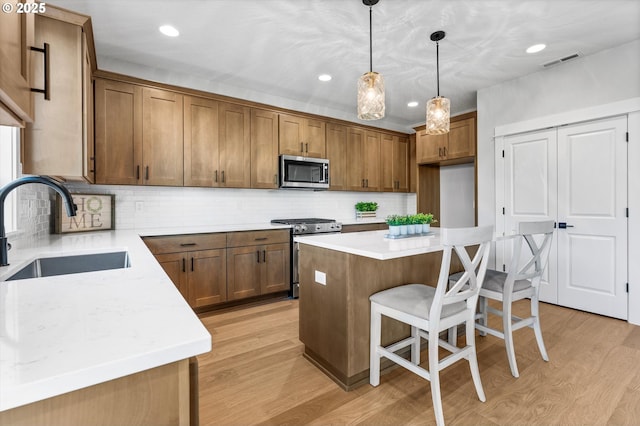 kitchen with stainless steel appliances, sink, decorative light fixtures, a center island, and light hardwood / wood-style floors