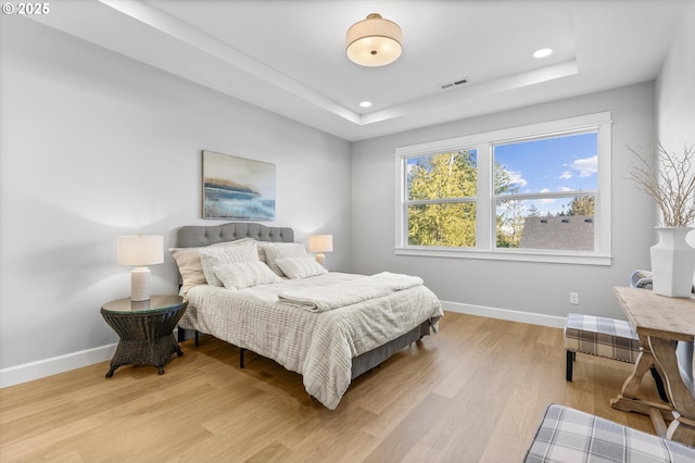 bedroom with a raised ceiling and light wood-type flooring