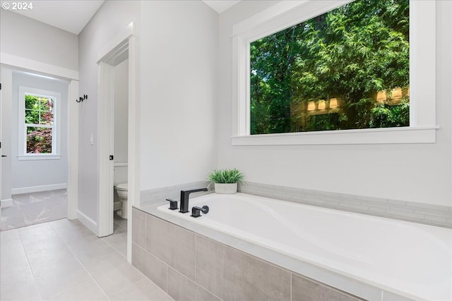 bathroom featuring tile patterned flooring, tiled tub, and toilet