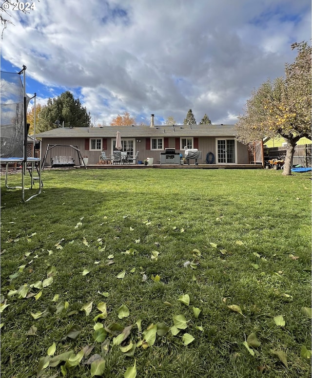 back of property featuring a wooden deck, a trampoline, and a yard