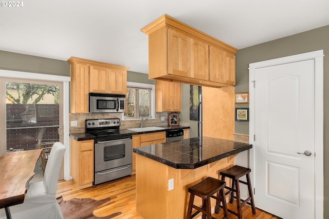 kitchen featuring light brown cabinetry, sink, light hardwood / wood-style flooring, kitchen peninsula, and stainless steel appliances