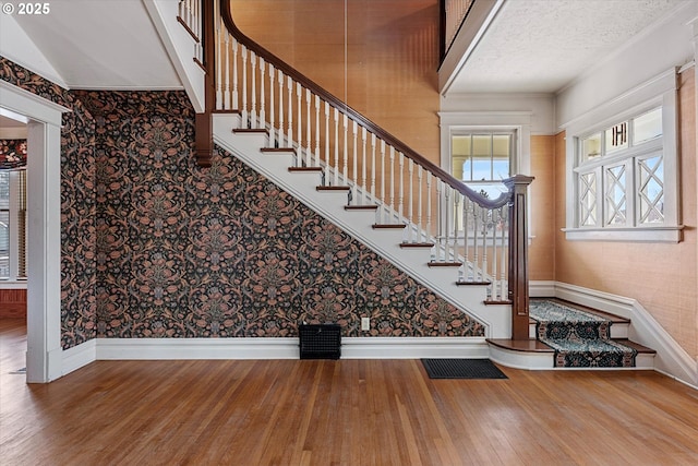 stairs with a textured ceiling, wallpapered walls, baseboards, and wood finished floors