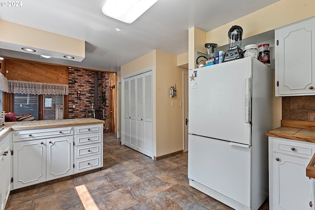 kitchen featuring white cabinets, white fridge, tile counters, and a wood stove