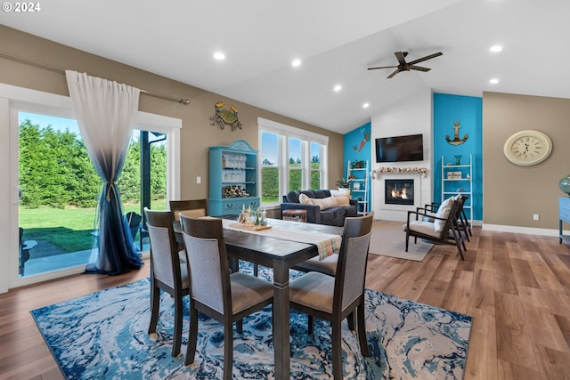 dining room featuring a wealth of natural light, a large fireplace, wood-type flooring, and vaulted ceiling