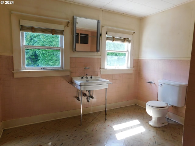 bathroom featuring a healthy amount of sunlight, toilet, parquet floors, and tile walls