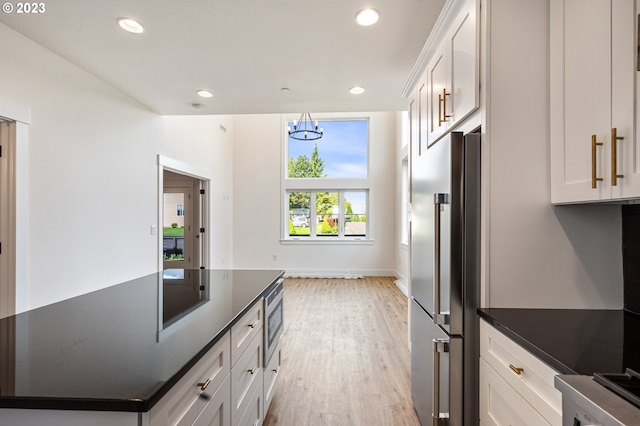 kitchen featuring an inviting chandelier, light hardwood / wood-style floors, stainless steel appliances, white cabinetry, and dark stone countertops