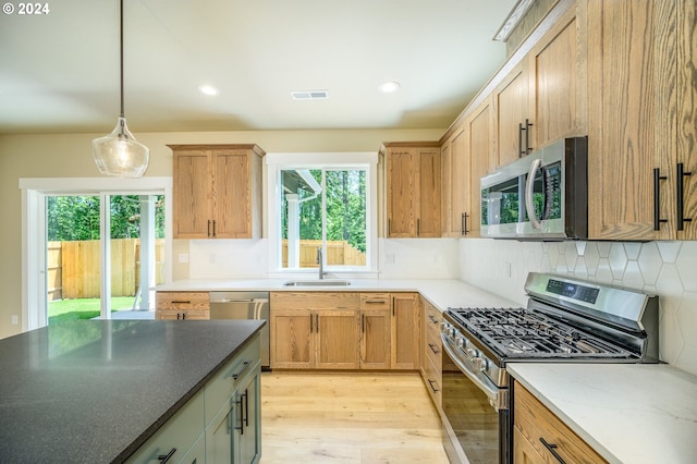 kitchen featuring appliances with stainless steel finishes, decorative light fixtures, sink, tasteful backsplash, and light hardwood / wood-style floors