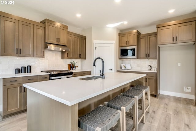 kitchen featuring a breakfast bar, a kitchen island with sink, sink, light hardwood / wood-style floors, and stainless steel appliances